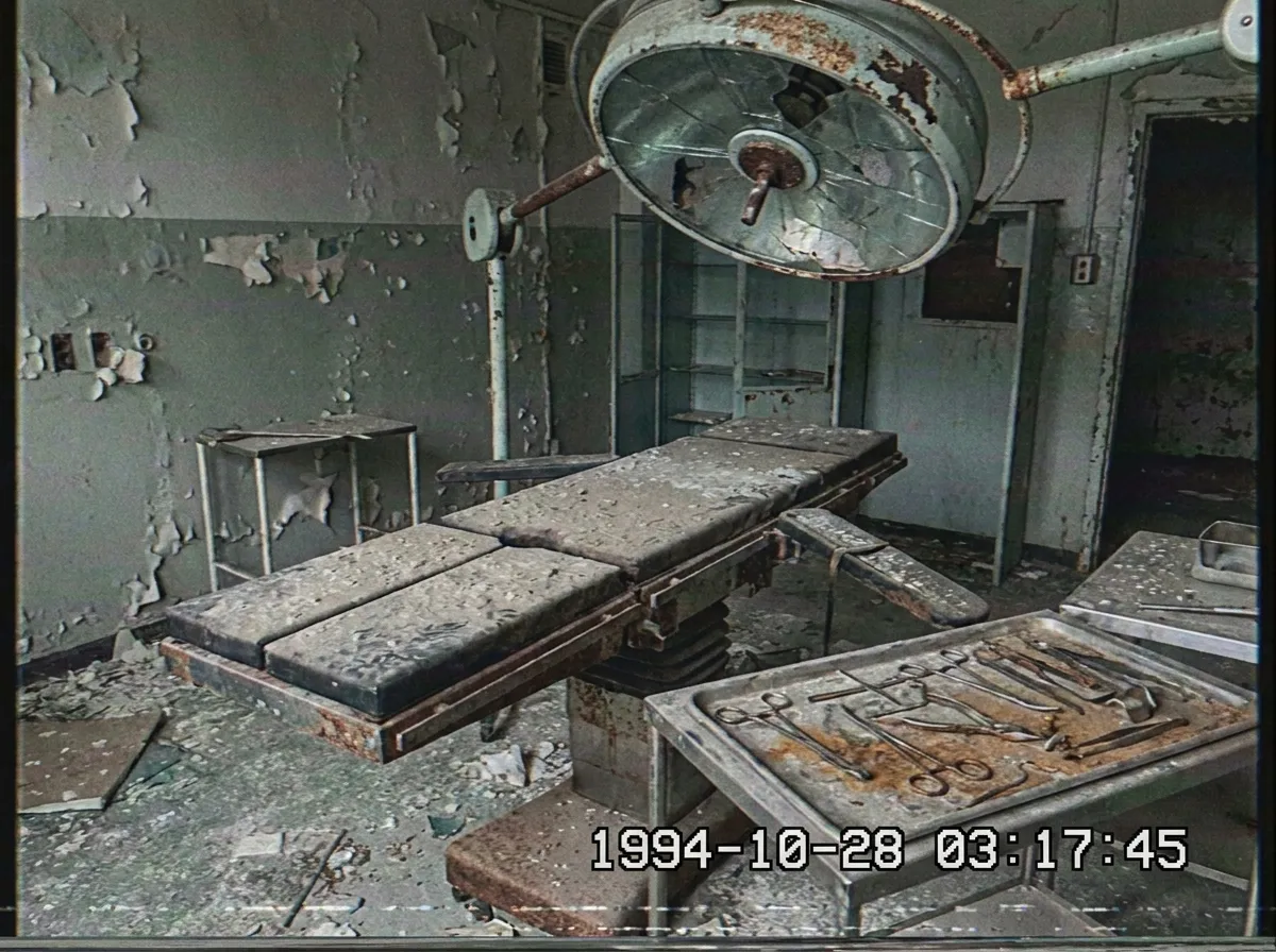 An abandoned surgical theatre with a rusted operating table beneath a cracked overhead lamp.